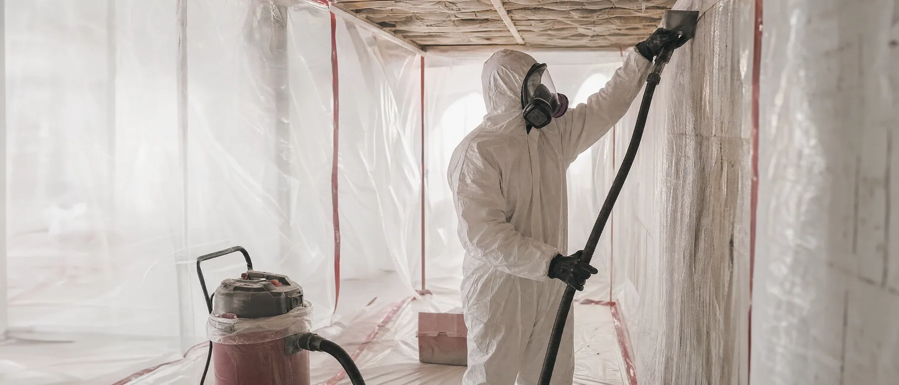 Abatement worker in a protective suit inside plastic containment during asbestos removal